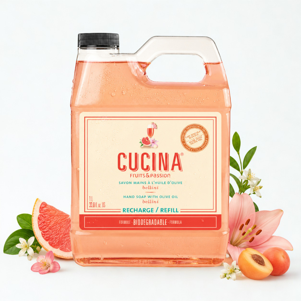 A large plastic jug of CUCINA Fruits & Passion hard soap refill filled with peach-colored liquid, surrounded by grapefruit, pink lilies, and apricots on a clean white background.