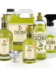 A set of Cucina Fruits & Passion olive oil products on a white background, including a large jug, a bottle, a spray bottle, a smaller bottle, a metal funnel, and a label.